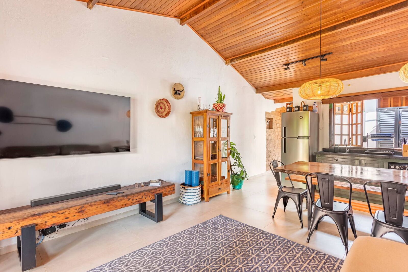 Sala de estar e cozinha integradas, com teto de madeira, Smart TV e vitrine antiga