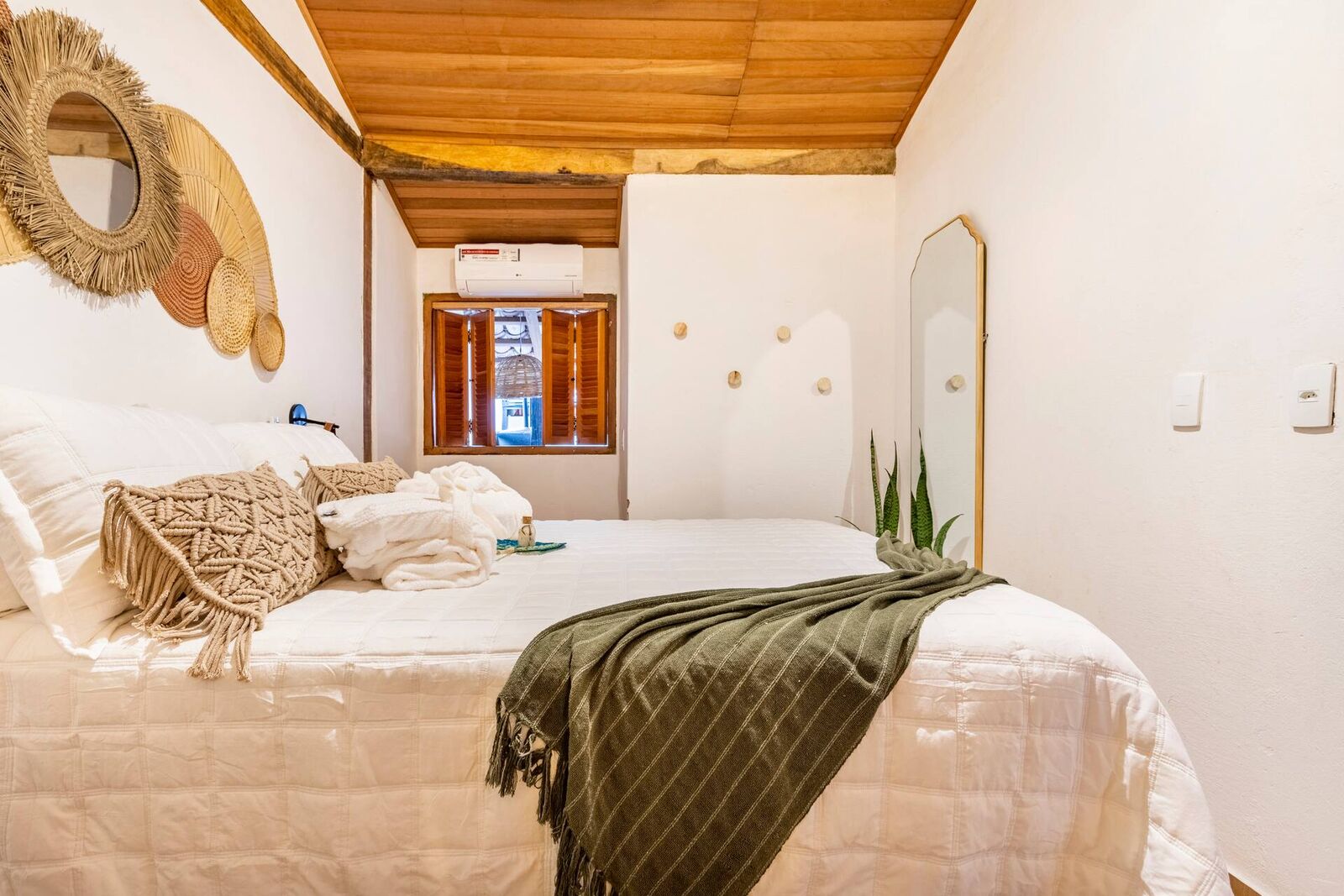 Suíte da Casa Boutique com cama queen, manta verde e espelhos de palha na parede