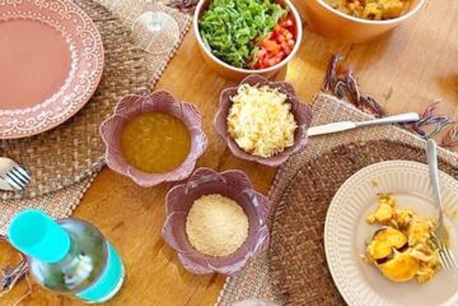 Mesa de madeira posta com pratos coloridos de cerâmica, farofa, vinagrete e um prato quente