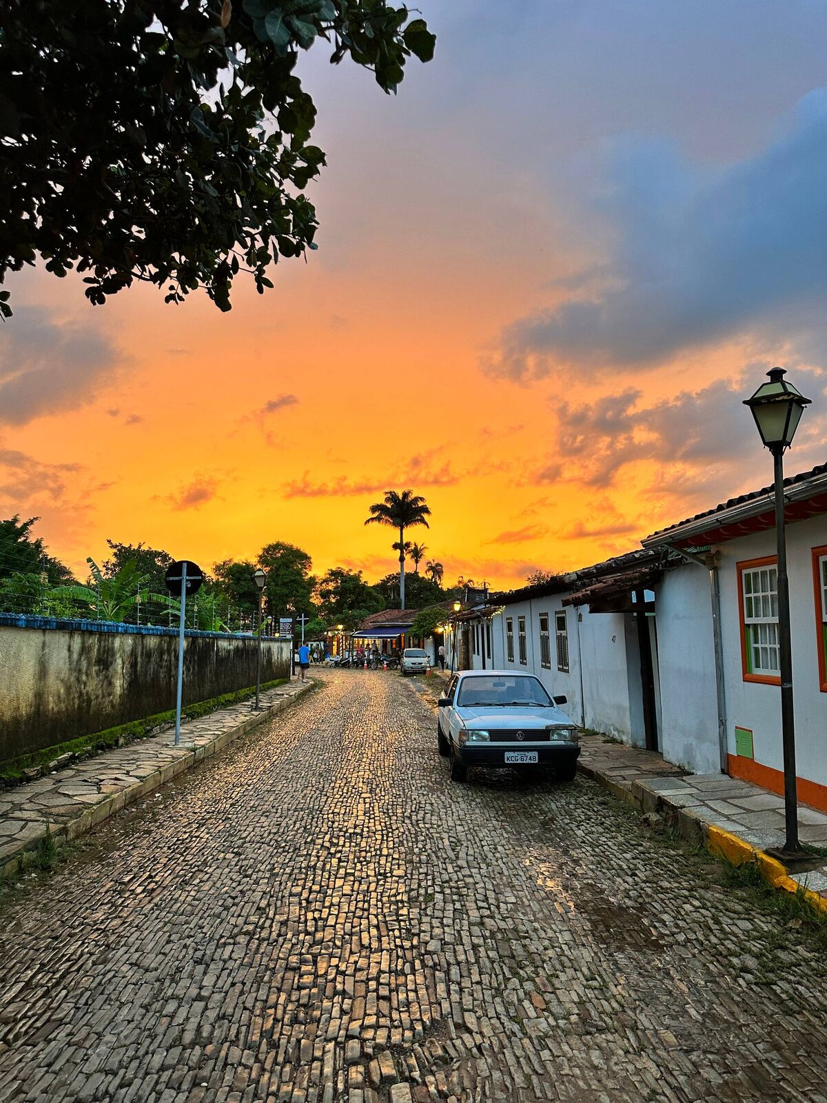 Pôr do sol alaranjado sobre uma rua de pedra do centro histórico de Pirenópolis, com poste antigo e casas coloniais